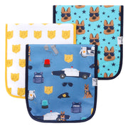 Three square baby bibs with rounded corners displayed in a fan arrangement on a white background. The front bib is light blue with a police-themed pattern including a dog, police car, badge, hat, and sunglasses.