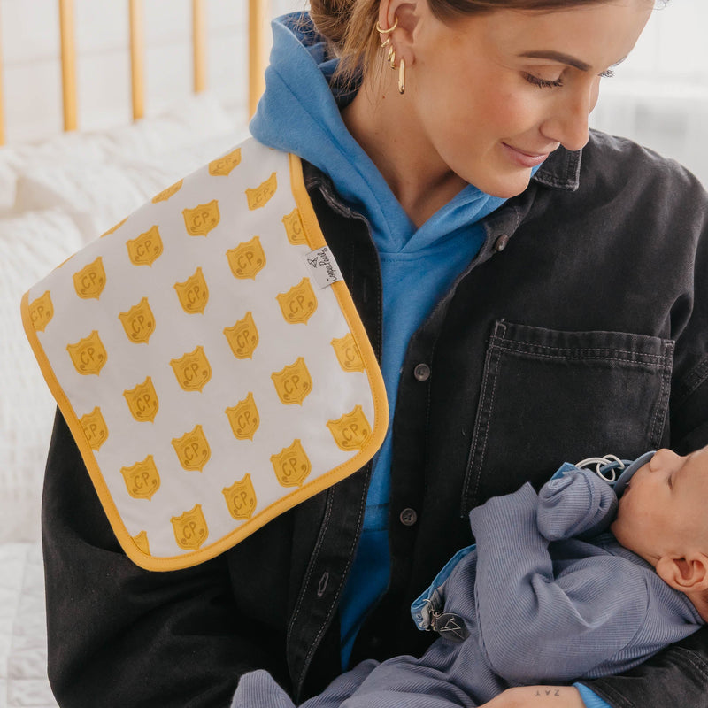 A woman in a black denim jacket and blue hoodie holds a baby wearing a blue onesie while wearing a white bib with yellow cat-face patterns and a yellow border.