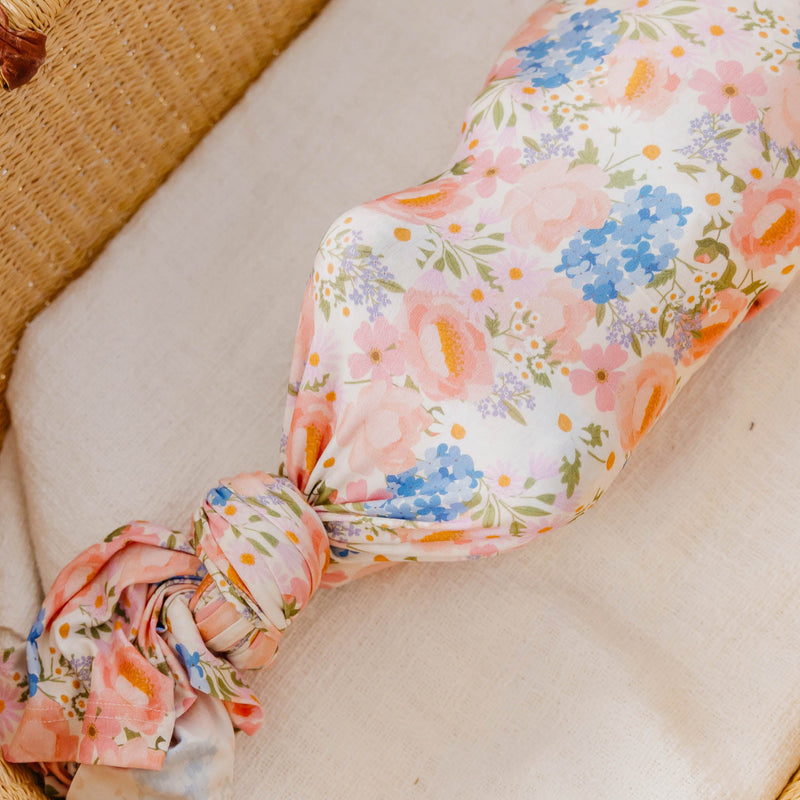A close-up of a floral fabric pouch tied in a knot, resting on a cream-colored cushion with a woven straw surface in the background.