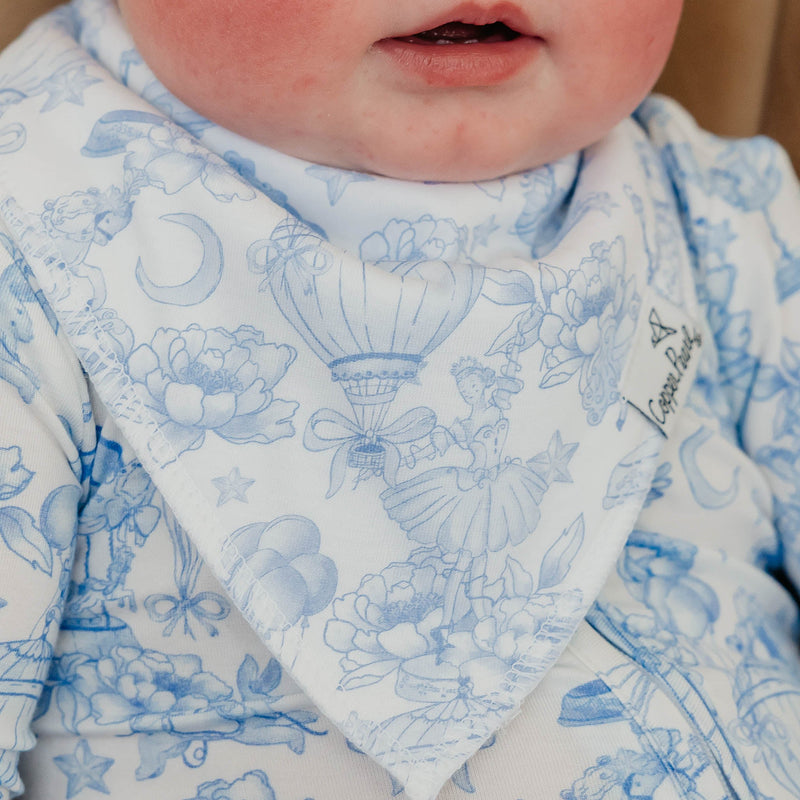 Close-up of a baby wearing a white bib with a light blue floral and hot air balloon pattern, paired with a matching blue patterned top.