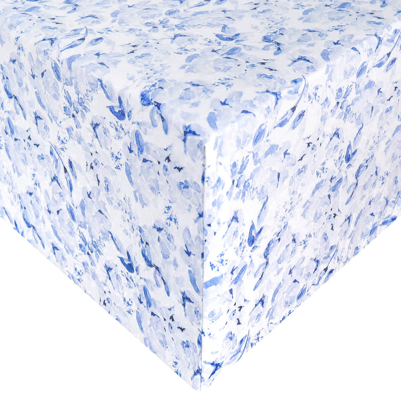 A close-up of a white tablecloth or fabric surface with an allover blue floral print, showing the corner and draped edges against a white background.
