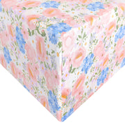 A close-up of a gift box wrapped in white wrapping paper featuring a pastel floral print with pink, blue, peach, and green flowers.