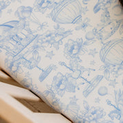 A close-up of a white wallpaper or fabric featuring a delicate blue toile-style pattern with hot air balloons, flowers, stars, and whimsical illustrations.