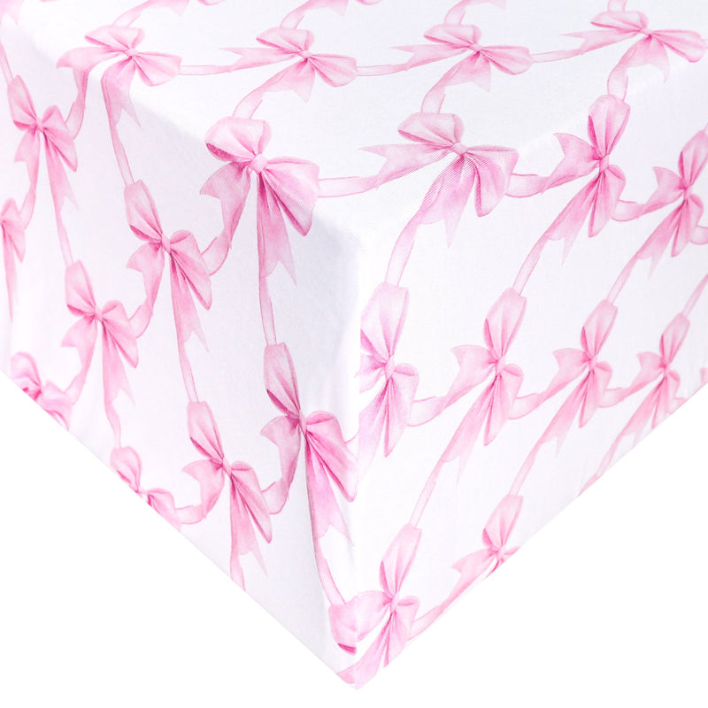 White gift wrap or fabric featuring a repeating pattern of pink ribbon bows, shown folded to display the design.