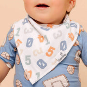 Baby wearing a bib with numbers and sports-themed clothing on a beige background
