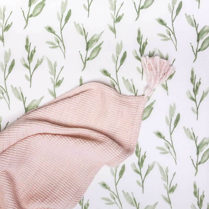 Pink fabric with tassel on a white background with green leaf pattern