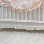 Close-up of a crib with striped crib sheet and lace trim