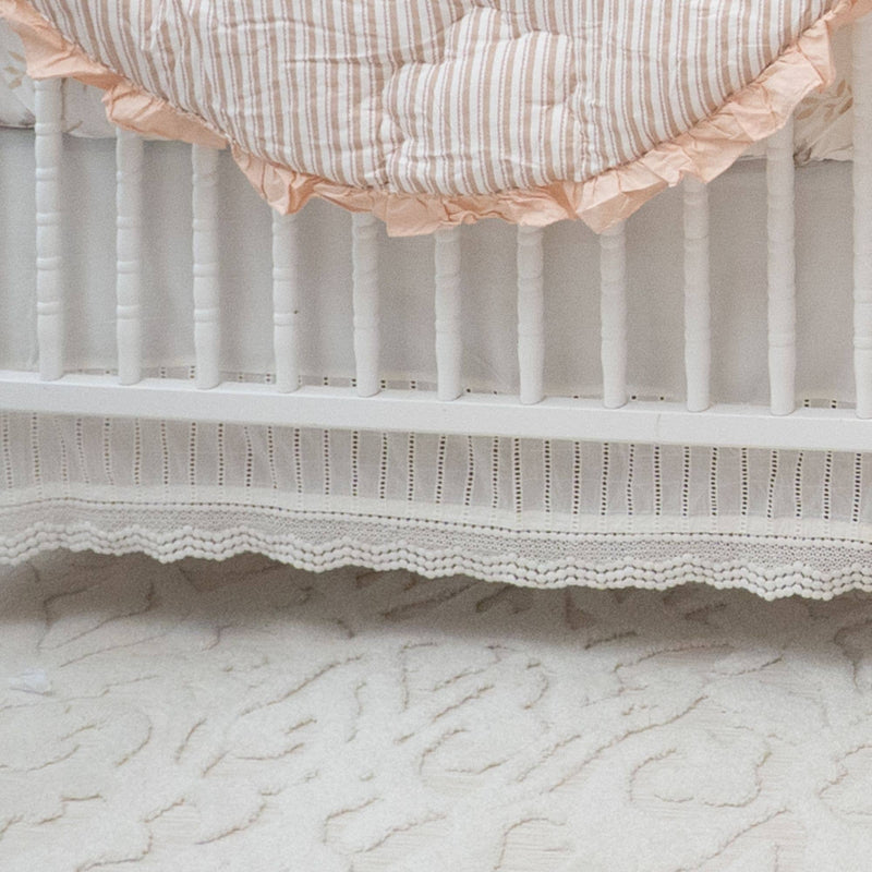 Close-up of a crib with striped crib sheet and lace trim