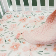 Parker Floral fitted crib sheet on mattress inside a white crib with quilt draped on the side