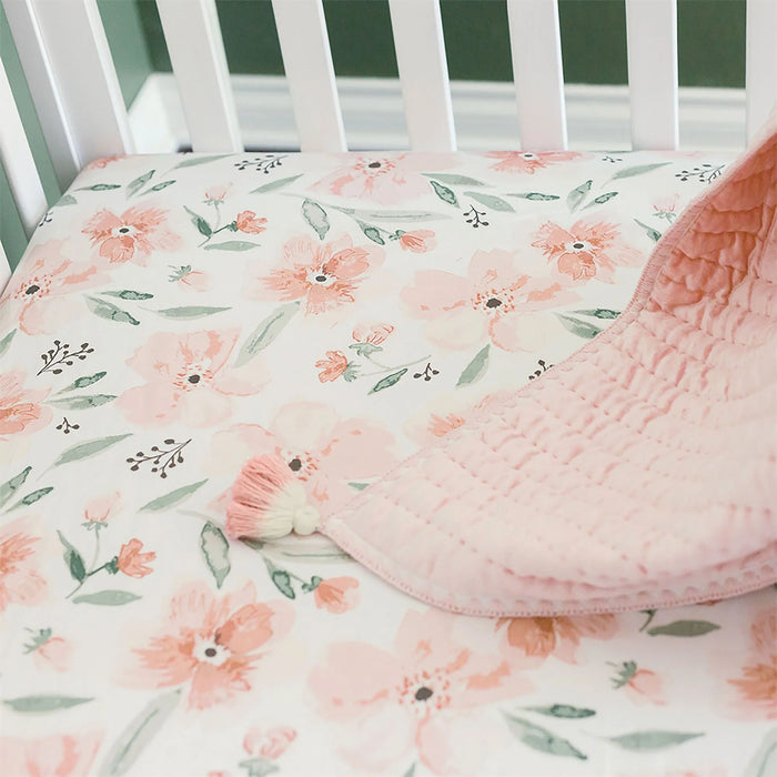 Parker Floral fitted crib sheet on mattress inside a white crib with quilt draped on the side
