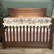 Wooden crib with floral bumper and pink bedding against a green wall.