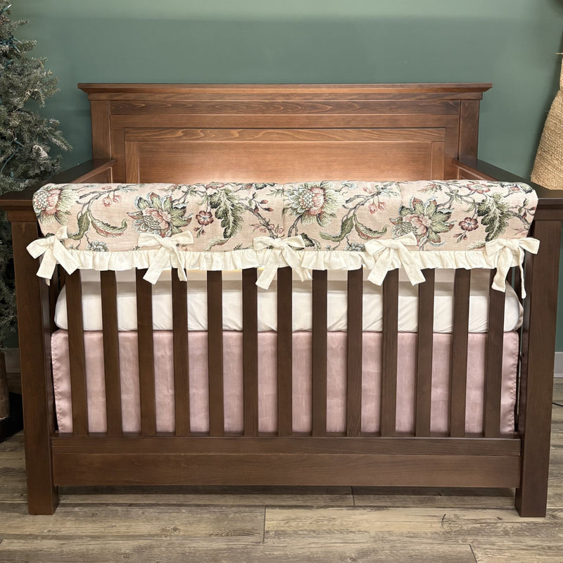 Wooden crib with floral bumper and pink bedding against a green wall.