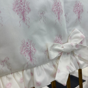 White fabric chair cover with a pink rose bouquet pattern and a ruffled hem, tied with a matching bow, shown on a wooden chair.