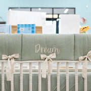 Crib with green bedding and 'Dream' text in a nursery setting