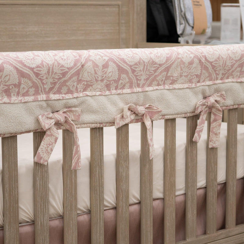 Pink and cream teething crib rail cover on a beige crib