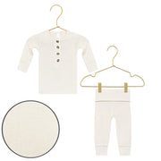 A baby two-piece knit outfit set in cream/off-white, featuring a long-sleeve henley top with three front buttons and matching pants, displayed on gold wire hangers against a white background, with a circular fabric detail inset.
