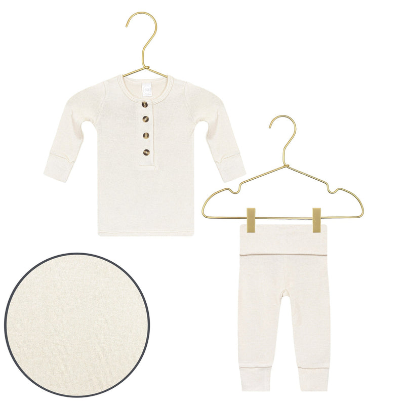 A baby two-piece knit outfit set in cream/off-white, featuring a long-sleeve henley top with three front buttons and matching pants, displayed on gold wire hangers against a white background, with a circular fabric detail inset.