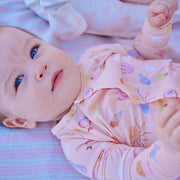 Baby lying on a striped blanket wearing a pink outfit with sea creature patterns.