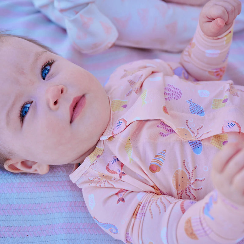 Baby lying on a striped blanket wearing a pink outfit with sea creature patterns.
