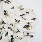 Flatlay of Saltwater Swaddles Diving Ducks crib sheet featuring detailed hand-painted ducks in flight on soft white cotton jersey