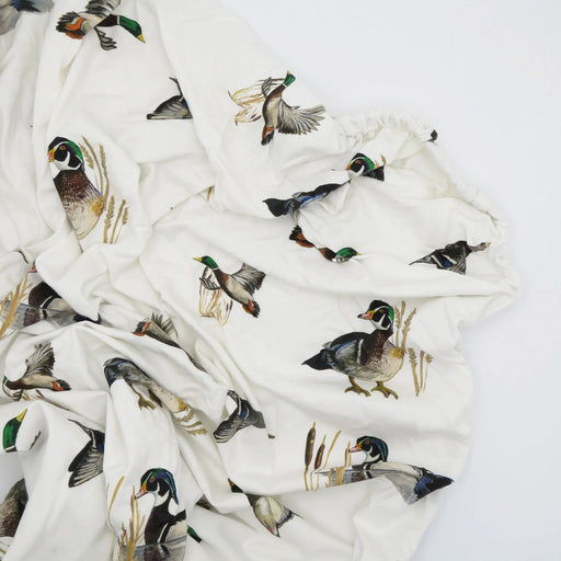 Flatlay of Saltwater Swaddles Diving Ducks crib sheet featuring detailed hand-painted ducks in flight on soft white cotton jersey
