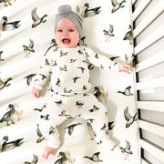 Baby lying on Saltwater Swaddles Diving Ducks crib sheet with illustrated ducks and neutral nature-inspired design