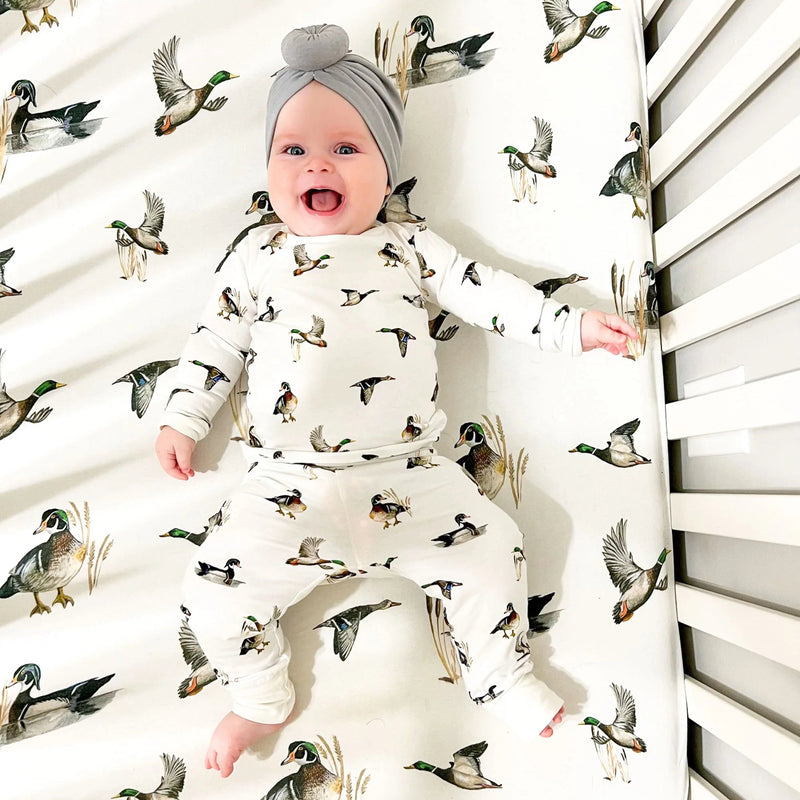 Baby lying on Saltwater Swaddles Diving Ducks crib sheet with illustrated ducks and neutral nature-inspired design