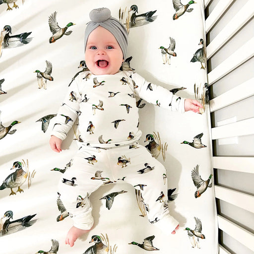 Baby lying on Saltwater Swaddles Diving Ducks crib sheet with illustrated ducks and neutral nature-inspired design