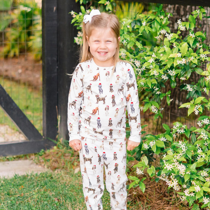 Child wearing Saltwater Swaddles Santa Dogs holiday pajamas standing outside surrounded by greenery