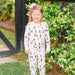Child wearing Saltwater Swaddles Santa Dogs holiday pajamas standing outside surrounded by greenery