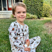 Child sitting on grass wearing Saltwater Swaddles Santa Dogs pajamas with festive dog print