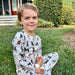 Child sitting on grass wearing Saltwater Swaddles Santa Dogs pajamas with festive dog print