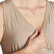 Woman wearing a beige sleeveless top with a necklace, on a plain background