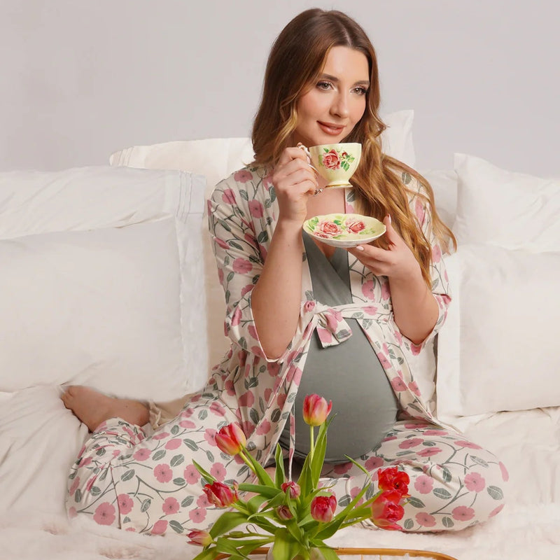 Woman sitting on a couch holding a teacup with a tray of tea and cupcakes in front of her.