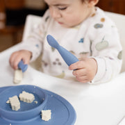 Toddler using an Indigo ezpz Tiny Spoon with an ezpz mat for baby-led weaning