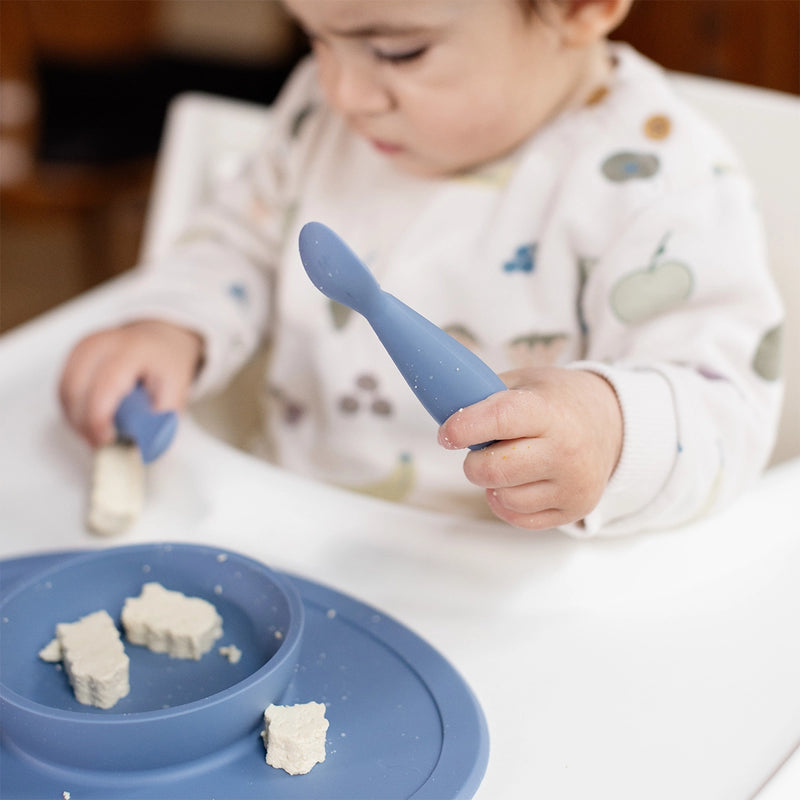 Toddler using an Indigo ezpz Tiny Spoon with an ezpz mat for baby-led weaning