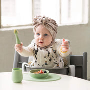 Baby holding a Sage ezpz Tiny Spoon at the table with matching bowl, mat and cup