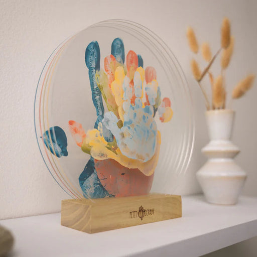 Decorative item with colorful handprint design on a stand, placed on a shelf.