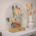 Decorative item with colorful handprint design on a stand, placed on a shelf.