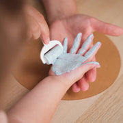 Child's hand holding a small blue sandcastle mold on a wooden surface
