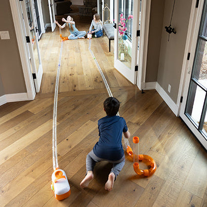 Child playing with air toobz on a wooden floor in a home setting.