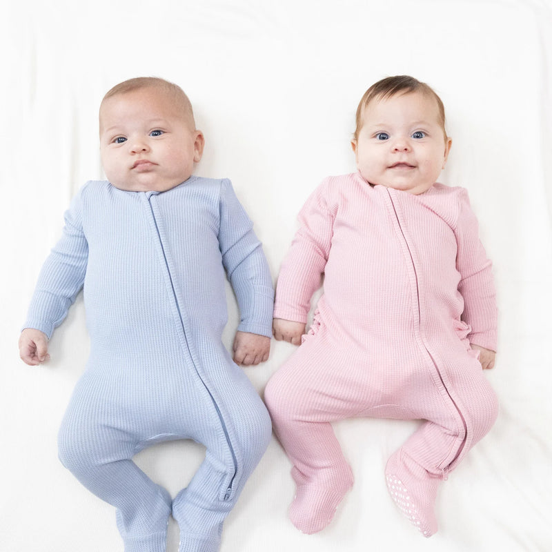 Two babies wearing the footies, one in blue and one in pink.