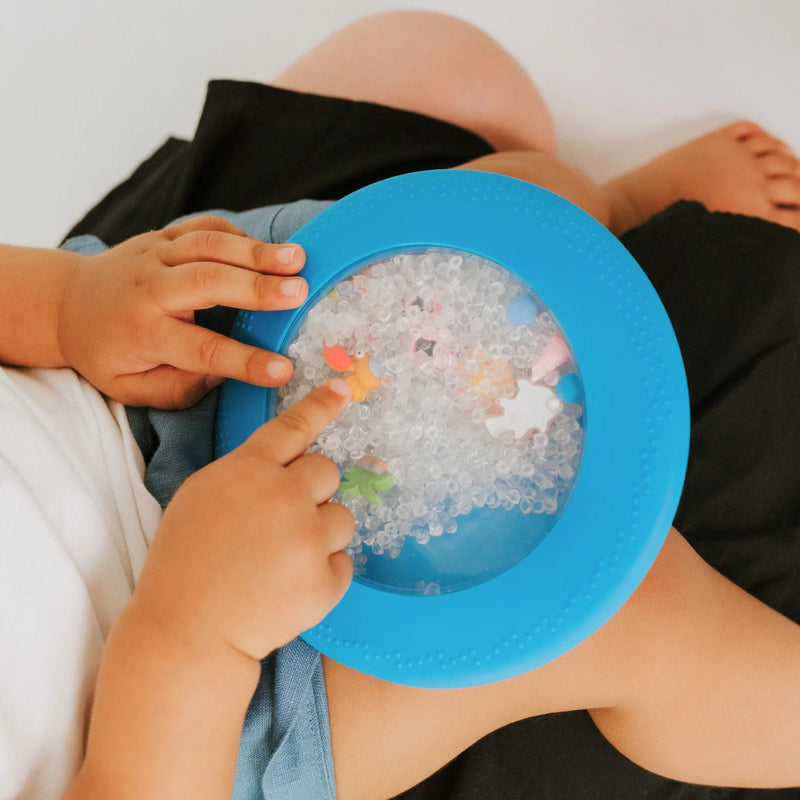 baby squeezing the blue peekaboo sensory bag during floor play