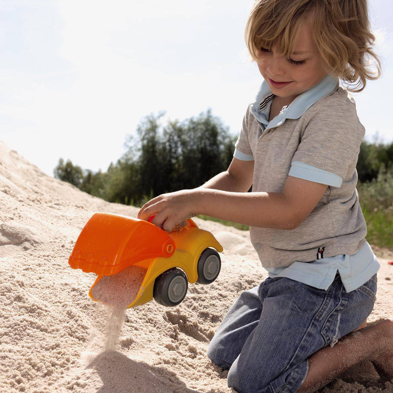 Child playing with a toy dump truck in the sand outdoors