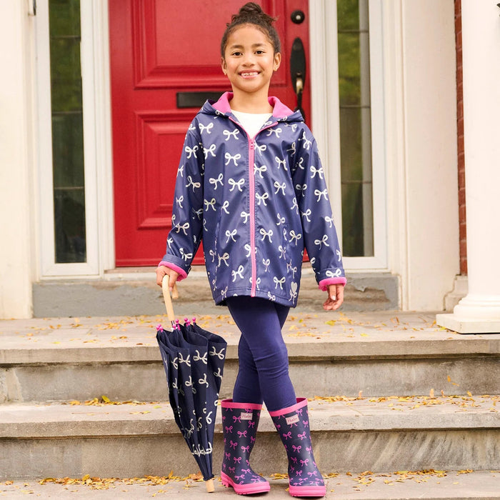 Child wearing navy foil bows rain jacket with matching boots on steps