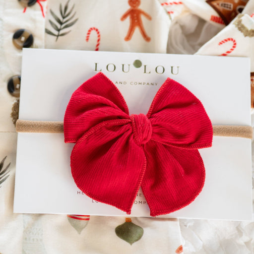 Red corduroy bow hair accessory on a white card with 'LOULOU' branding, set against a festive background.