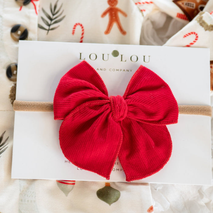 Red corduroy bow hair accessory on a white card with 'LOULOU' branding, set against a festive background.
