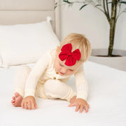 Baby wearing a red heirloom bow on a white bed