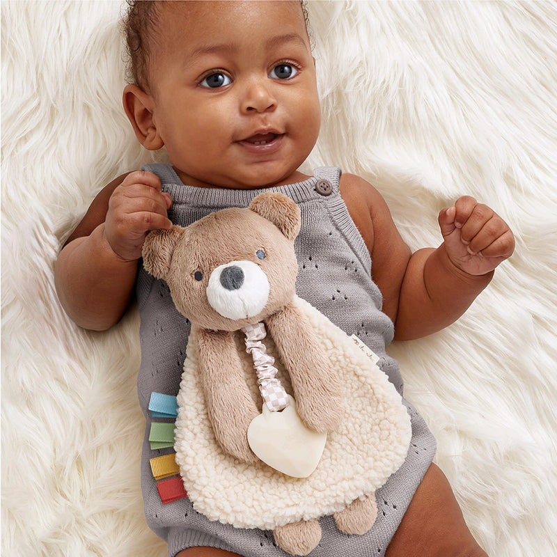 Smiling baby lying on a fluffy rug holding the Itzy Ritzy Theo the Bear lovey