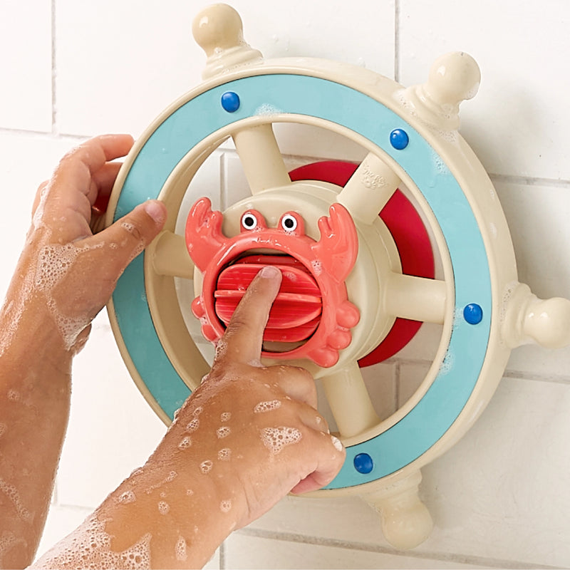 Child's hand turning a colorful toy steering wheel with a crab handle, a tile wall